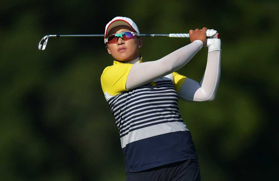 梁熙英全神贯注地跪在果岭边，目光如炬地审视着推杆线路，仿佛在解读大地隐秘的脉络