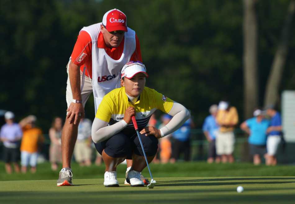 梁熙英与同组球员史黛西在果岭上并肩观察推杆线路，两位顶尖高手正在上演一场无声的智慧博弈