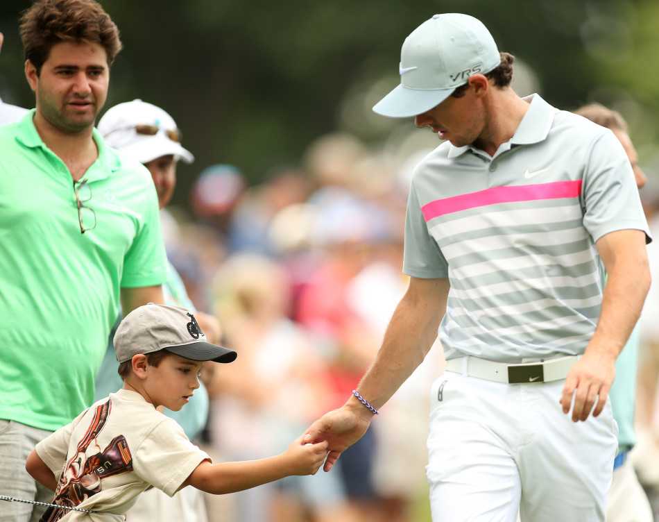 麦克罗伊弯下腰，将一颗高尔夫球递给围绳外兴奋不已的小球迷，笑容亲切