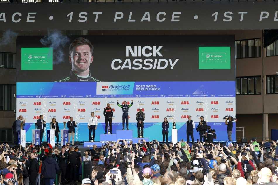 领奖台上，冠军卡西迪被香槟的欢腾金雨笼罩，他高举奖杯畅饮，笑容灿烂，尽情释放胜利的狂喜。