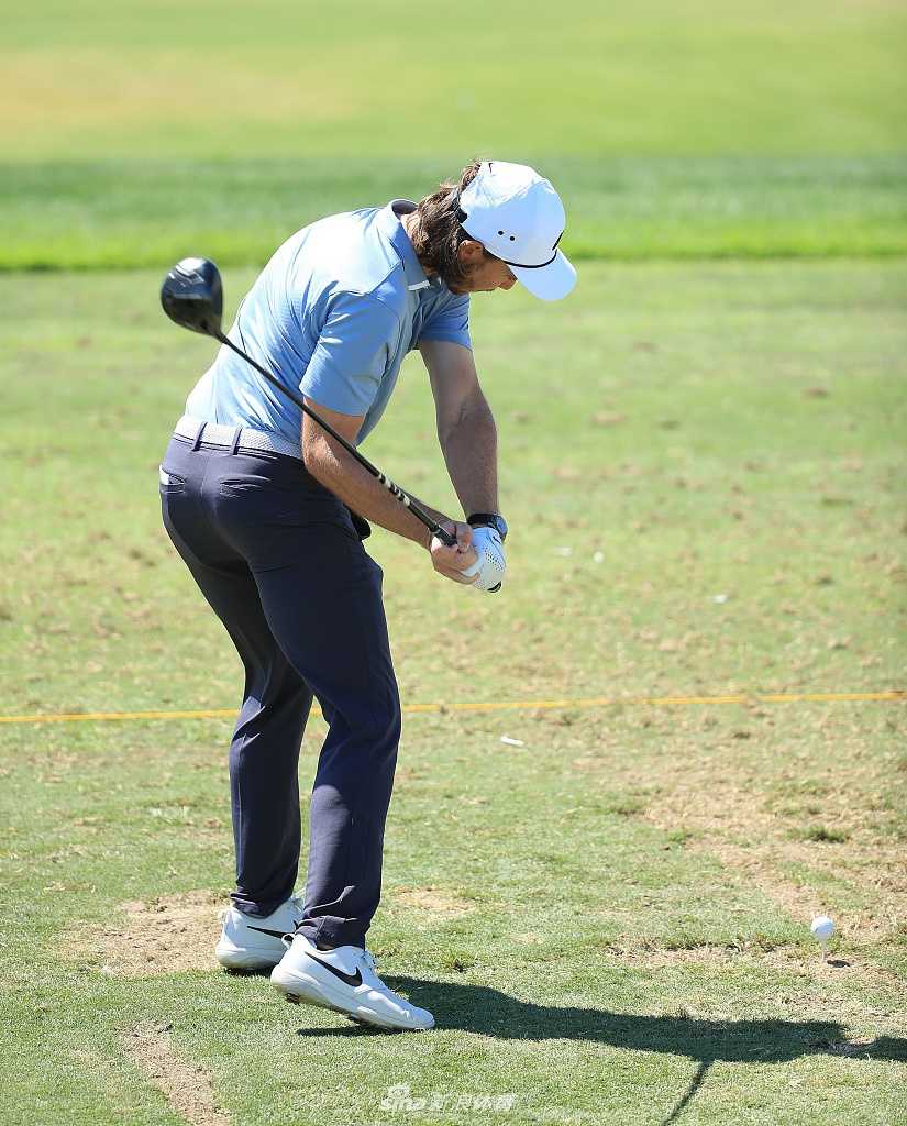 球场风景如画，宽阔的水障碍倒映着蓝天白云，球道向着远方延伸。