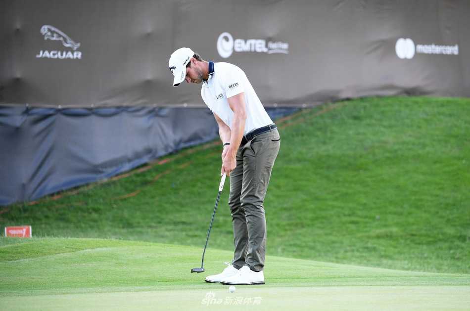 卡勒姆·希尔在果岭上仔细阅读推杆线路，他俯身观察的姿态与毛里求斯传承赛标志性的果岭环相映成趣。